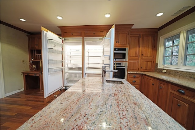 kitchen with dark wood-type flooring, sink, ornamental molding, stainless steel double oven, and light stone countertops