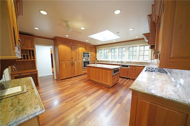 kitchen with a kitchen island, a skylight, light stone counters, stainless steel appliances, and crown molding