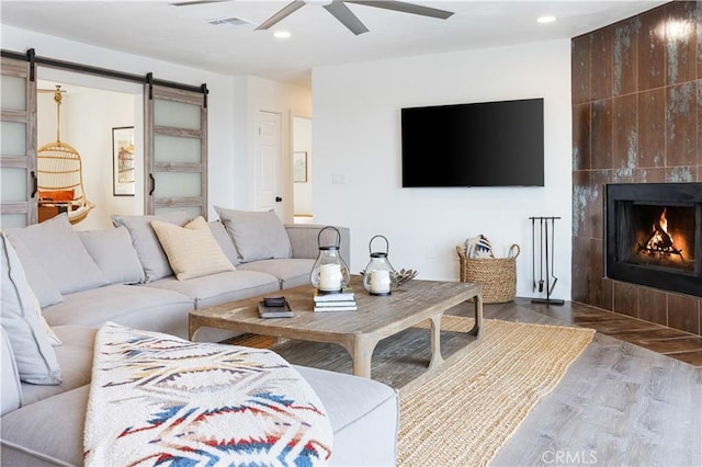 living room featuring a tile fireplace, hardwood / wood-style flooring, ceiling fan, and a barn door