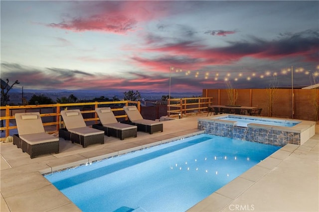 pool at dusk featuring an in ground hot tub and a patio area