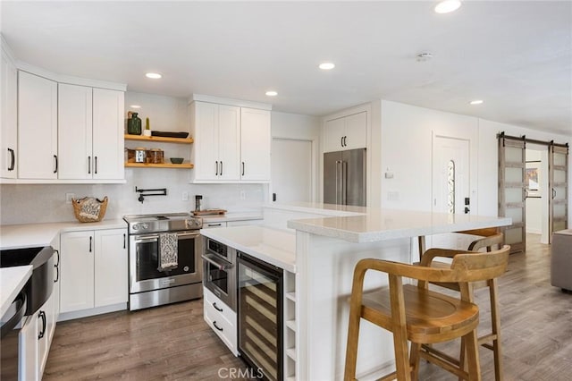 kitchen with premium appliances, a barn door, white cabinets, a breakfast bar, and wine cooler