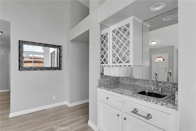 kitchen with light stone countertops, sink, white cabinetry, and light wood-type flooring