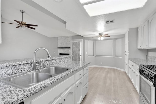 kitchen with sink, white cabinetry, stainless steel gas range, and light hardwood / wood-style flooring