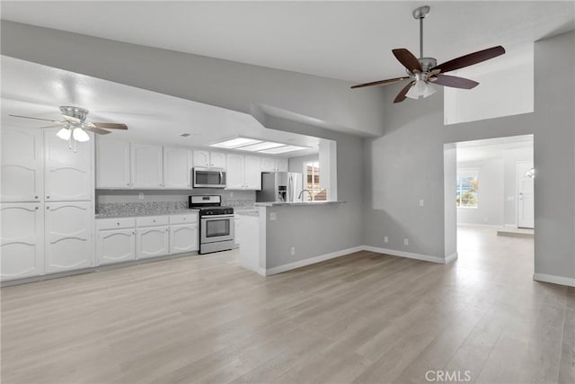 kitchen with light hardwood / wood-style floors, white cabinets, kitchen peninsula, stainless steel appliances, and lofted ceiling