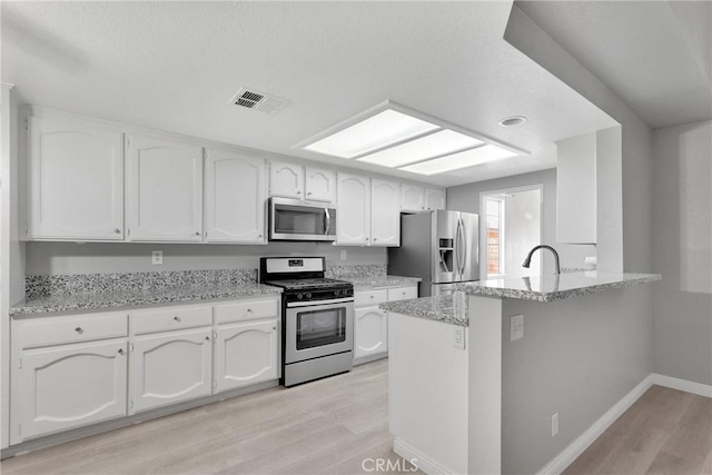 kitchen with appliances with stainless steel finishes, white cabinetry, light hardwood / wood-style flooring, kitchen peninsula, and light stone counters