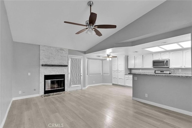 unfurnished living room featuring ceiling fan, a stone fireplace, light hardwood / wood-style floors, and high vaulted ceiling