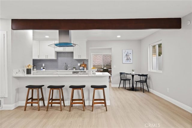 kitchen featuring a breakfast bar area, tasteful backsplash, island range hood, white cabinets, and kitchen peninsula