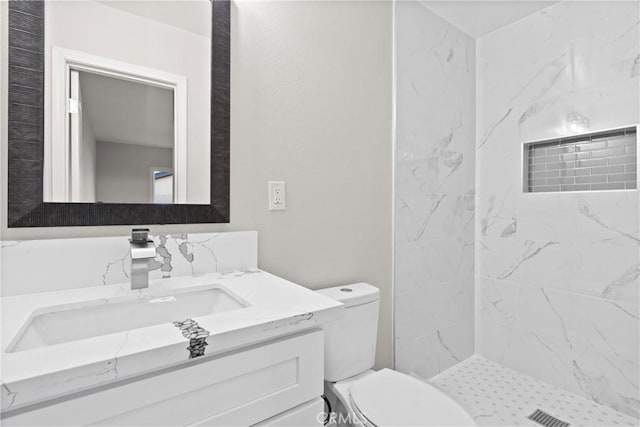 bathroom with vanity, tiled shower, and toilet