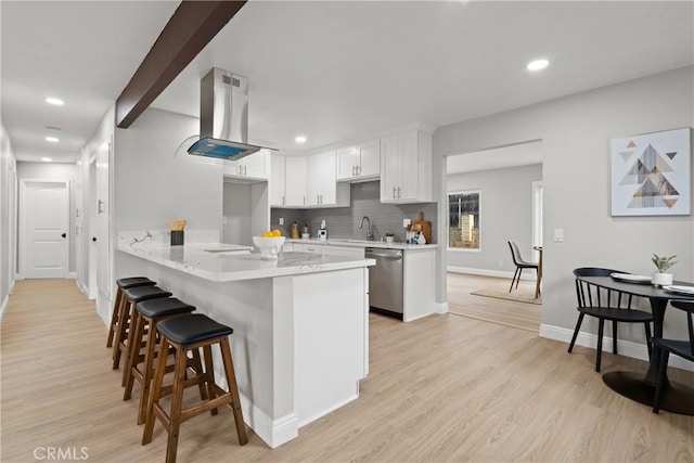 kitchen featuring island range hood, white cabinets, a kitchen bar, stainless steel dishwasher, and kitchen peninsula