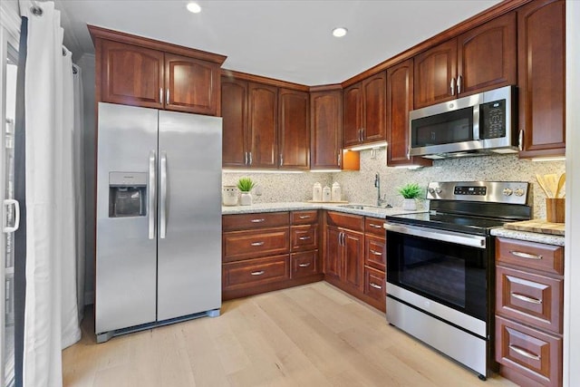 kitchen with sink, appliances with stainless steel finishes, light stone countertops, light hardwood / wood-style floors, and decorative backsplash