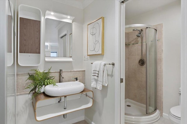 bathroom with toilet, ornamental molding, a shower with door, and sink