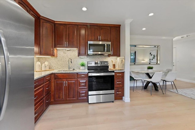 kitchen featuring sink, stainless steel appliances, ornamental molding, light stone countertops, and light wood-type flooring