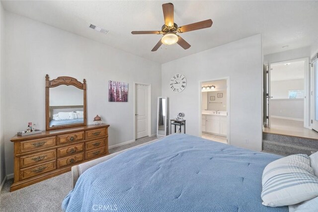 bedroom featuring ceiling fan, light colored carpet, and ensuite bath