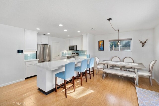 kitchen featuring white cabinets, stainless steel appliances, backsplash, hanging light fixtures, and a breakfast bar area