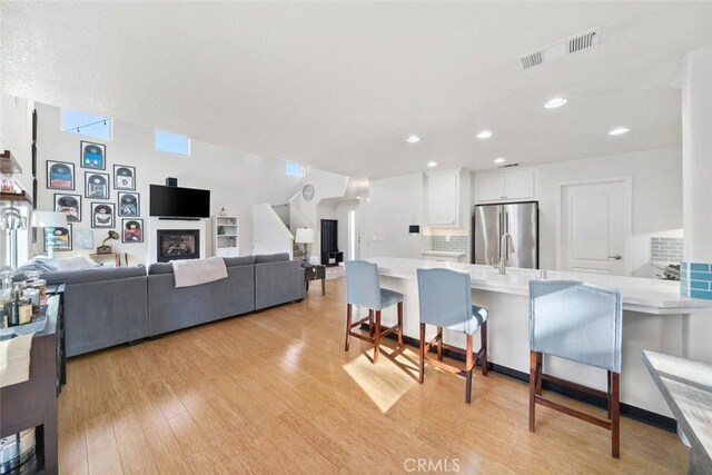 kitchen with white cabinetry, tasteful backsplash, a kitchen breakfast bar, stainless steel refrigerator, and light hardwood / wood-style flooring