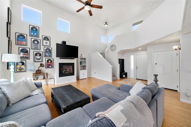 living room featuring a towering ceiling, ceiling fan, and light hardwood / wood-style flooring