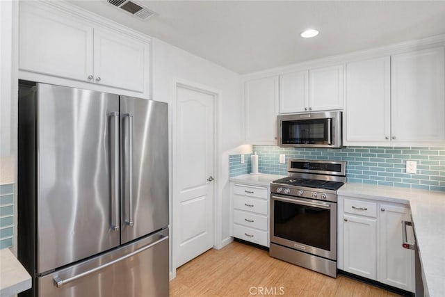 kitchen with backsplash, white cabinetry, light hardwood / wood-style flooring, and stainless steel appliances