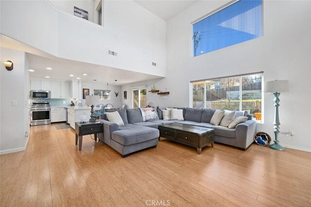 living room with light hardwood / wood-style floors, a towering ceiling, and plenty of natural light