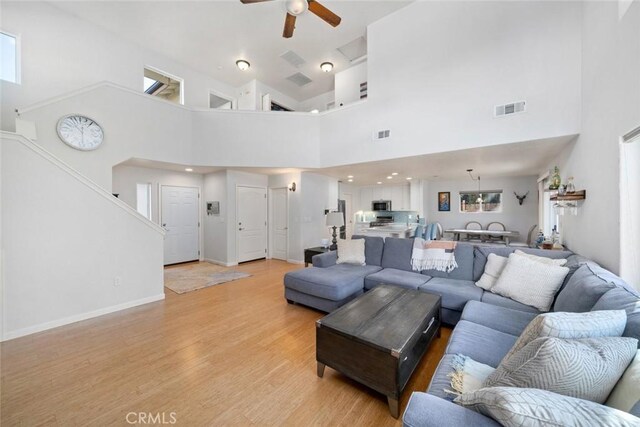 living room featuring light wood-type flooring, a towering ceiling, and ceiling fan