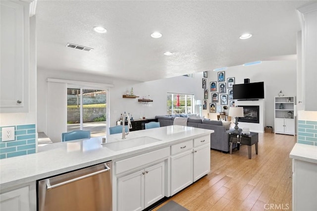 kitchen featuring a textured ceiling, tasteful backsplash, white cabinetry, stainless steel dishwasher, and sink