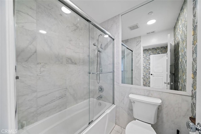 bathroom with toilet, enclosed tub / shower combo, and tile walls