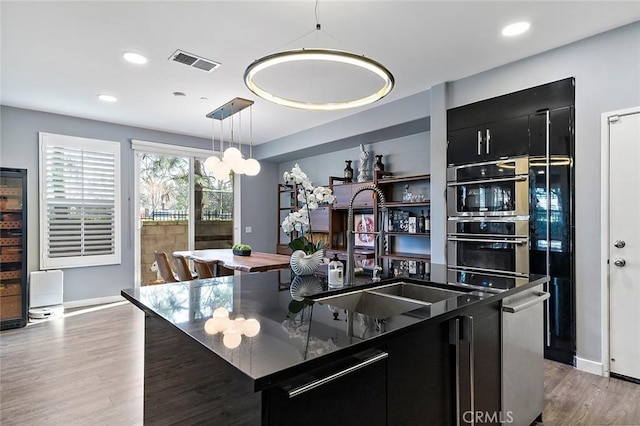 kitchen with light hardwood / wood-style flooring, decorative light fixtures, sink, a kitchen island with sink, and stainless steel appliances