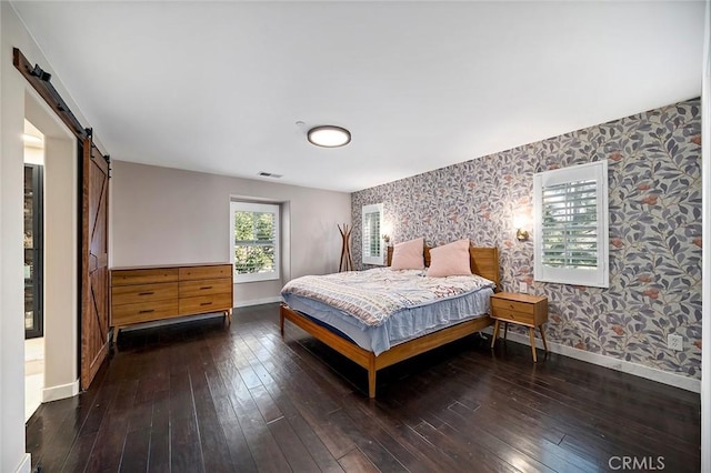 bedroom with a barn door and dark hardwood / wood-style flooring