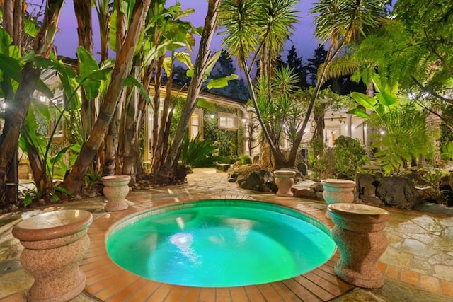 pool at dusk featuring a hot tub