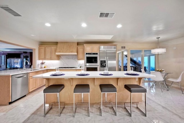 kitchen with appliances with stainless steel finishes, decorative backsplash, hanging light fixtures, a center island, and wall chimney range hood