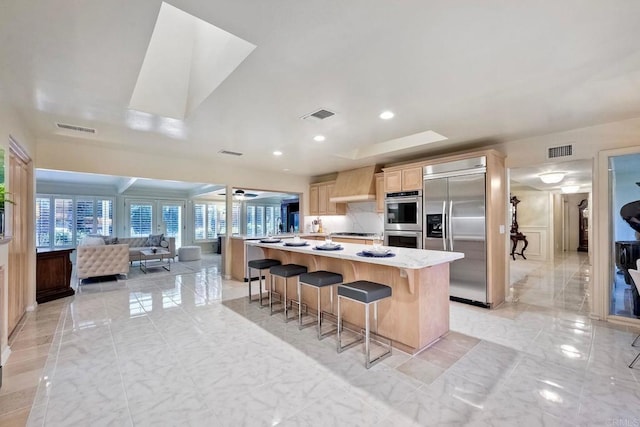 kitchen featuring wall chimney exhaust hood, a breakfast bar, light brown cabinets, a kitchen island, and stainless steel appliances