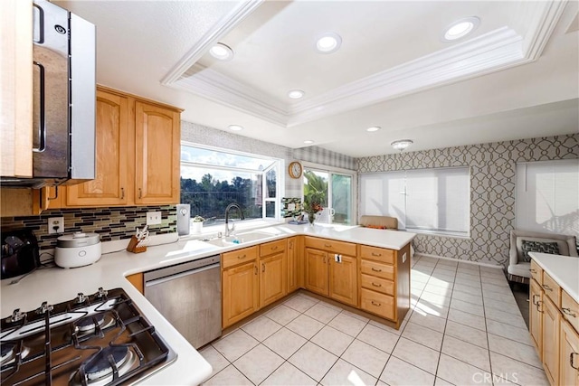 kitchen featuring sink, stainless steel dishwasher, ornamental molding, a tray ceiling, and kitchen peninsula