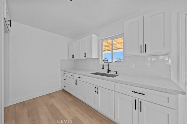 kitchen with backsplash, light hardwood / wood-style floors, sink, and white cabinets