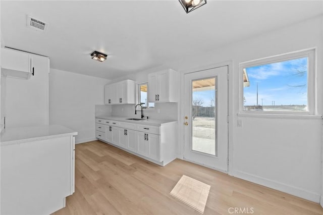 kitchen with backsplash, light hardwood / wood-style floors, sink, and white cabinets