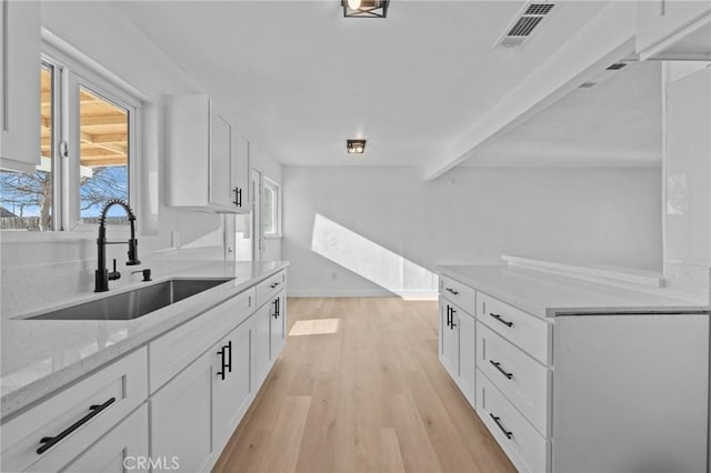 kitchen featuring beamed ceiling, white cabinetry, sink, light stone countertops, and light hardwood / wood-style flooring