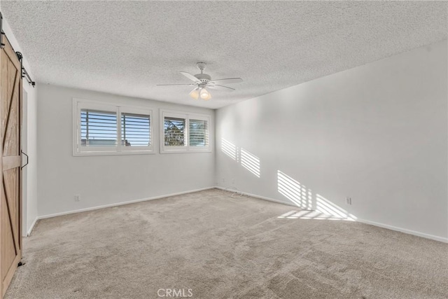 carpeted spare room with ceiling fan, a textured ceiling, and a barn door