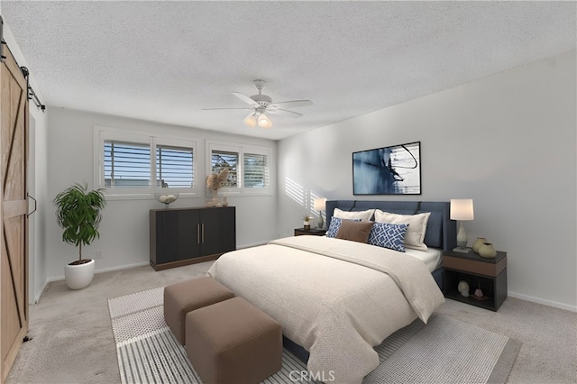 carpeted bedroom with ceiling fan, a barn door, and a textured ceiling