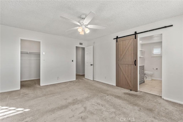 unfurnished bedroom featuring light carpet, ceiling fan, a walk in closet, connected bathroom, and a closet