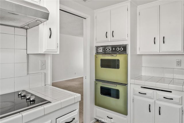 kitchen with multiple ovens, white cabinetry, and tile countertops