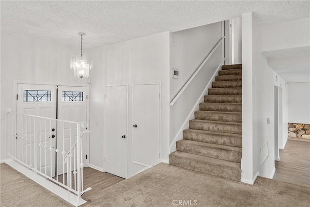 stairway featuring carpet flooring, a textured ceiling, and a notable chandelier