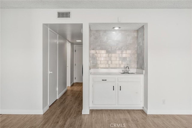 bar featuring light wood-type flooring, white cabinetry, decorative backsplash, and a textured ceiling