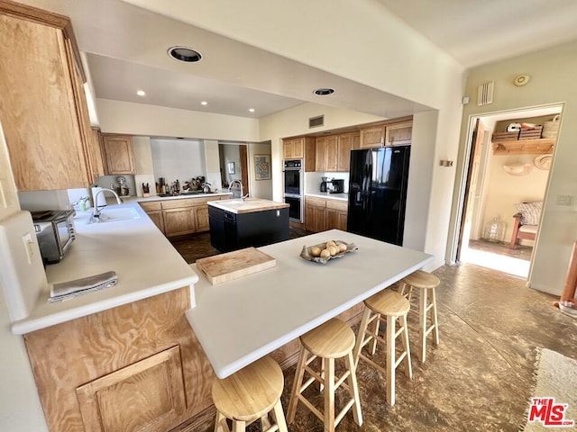 kitchen featuring black appliances, a kitchen island with sink, sink, and a kitchen bar