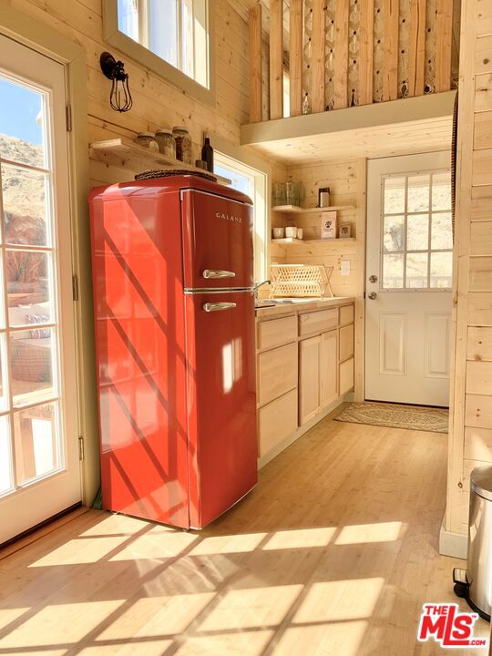 interior space featuring light wood-type flooring, a high ceiling, refrigerator, and wooden walls