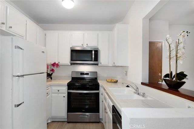 kitchen featuring hardwood / wood-style floors, white cabinets, appliances with stainless steel finishes, sink, and kitchen peninsula