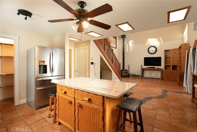 kitchen featuring a kitchen breakfast bar, stainless steel refrigerator with ice dispenser, light stone countertops, a kitchen island, and a wood stove