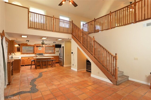 living room featuring light tile patterned flooring, a towering ceiling, sink, and ceiling fan