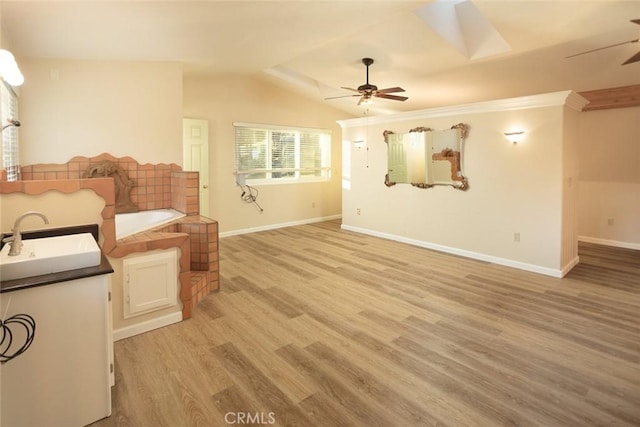 unfurnished living room featuring sink, vaulted ceiling with skylight, ceiling fan, and light hardwood / wood-style floors