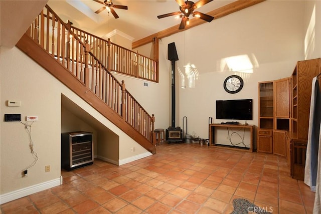 unfurnished living room with light tile patterned floors, ceiling fan, a towering ceiling, wine cooler, and a wood stove