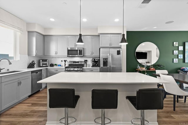 kitchen with stainless steel appliances, a kitchen island, gray cabinets, and decorative light fixtures