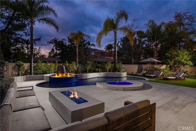 pool at dusk featuring an in ground hot tub, a patio, pool water feature, and an outdoor fire pit