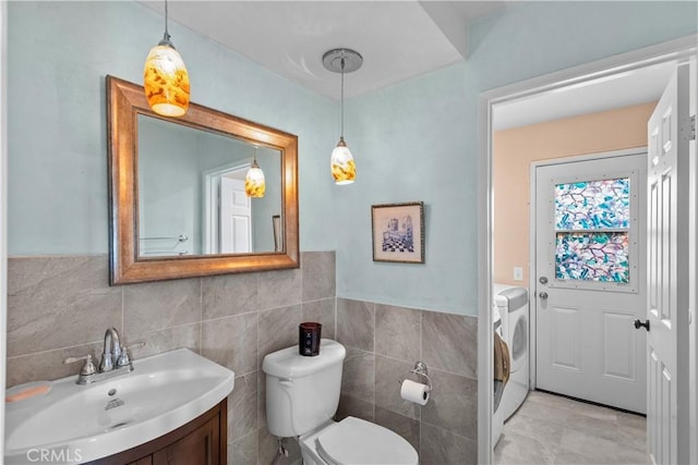 bathroom with tile walls, toilet, vanity, and washing machine and clothes dryer